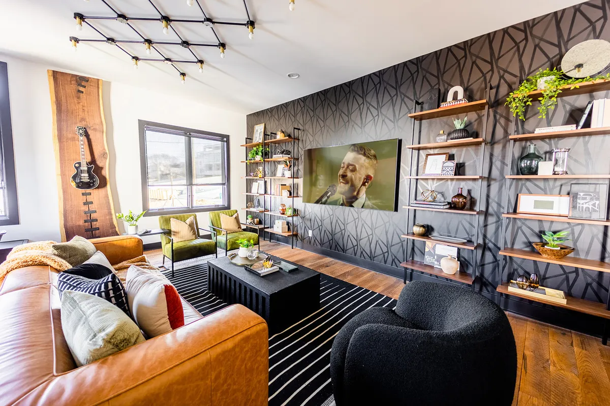 The image captures a vibrant and stylish living area featuring a guitar mounted on the wall, a large television playing a concert, chic shelving with decorative accents, and a plush sofa ideal for lounging and socializing. The contemporary décor hints at a lively Nashville vibe, perfectly suited for group gatherings and musical inspiration.