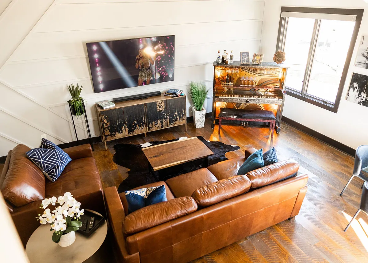 A welcoming living area featuring a leather sofa, piano, television, and coffee table. The atmosphere is warm, with elements that encourage music, conversation, and entertainment.