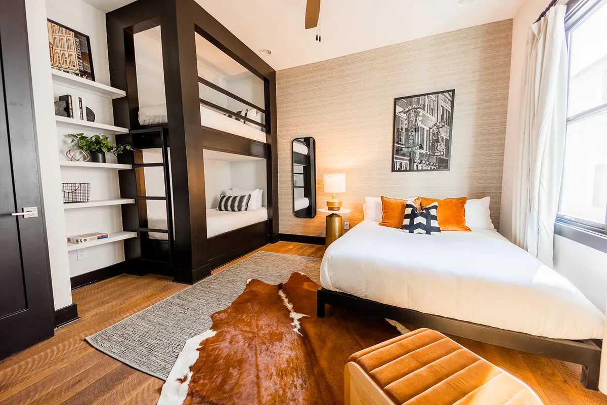 A bedroom with a combination of bunk beds and a queen bed, complete with a cowhide rug, playful artwork, and decorative pillows. The space is inviting, contemporary, and ideal for families or groups seeking both style and functionality.