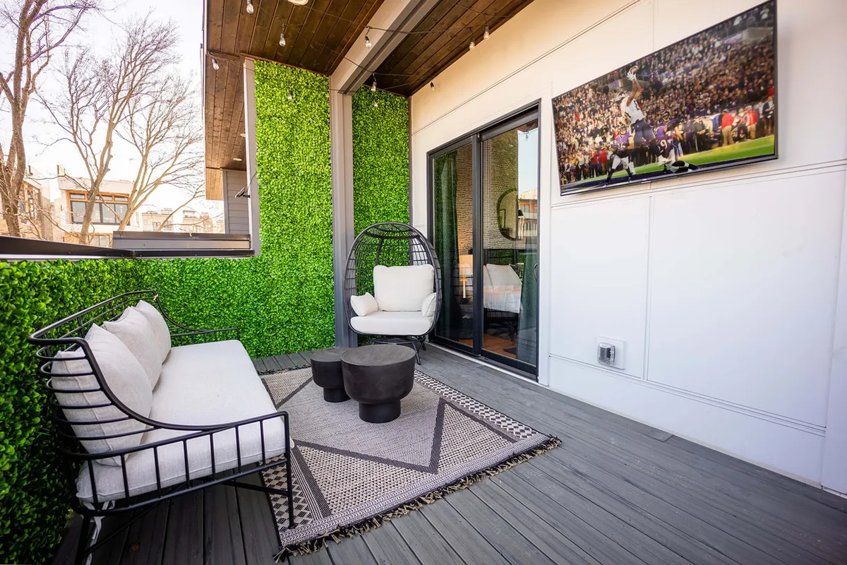 A rooftop lounge zone with a green wall, hanging chair, coffee table, and a prominent outdoor television screen. The scene is set for watching the big game or hosting a movie night under the stars, blending comfort and entertainment.