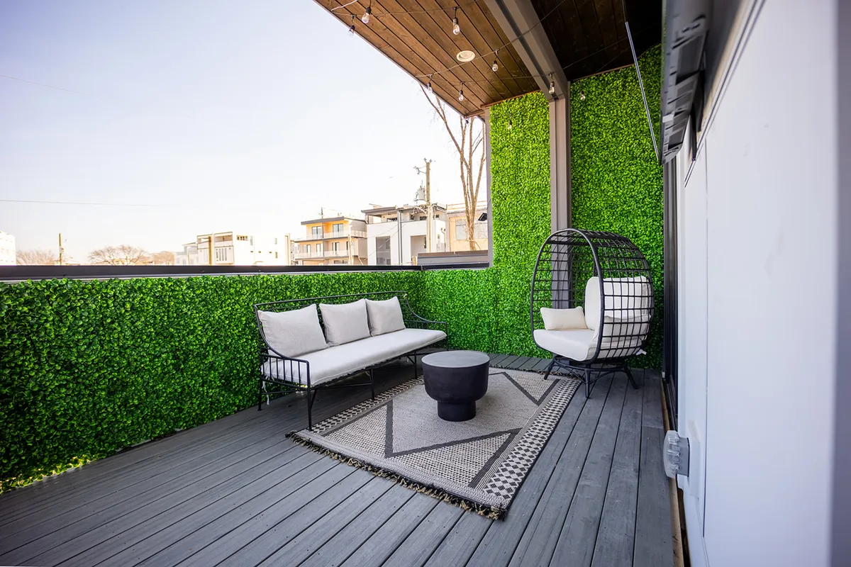 A lush rooftop patio with a greenery wall, hanging chair, comfortable sofa, and a circular coffee table, all set atop a decorative rug. The ambiance is serene, with string lights overhead creating an inviting atmosphere for socializing or unwinding after a productive day.
