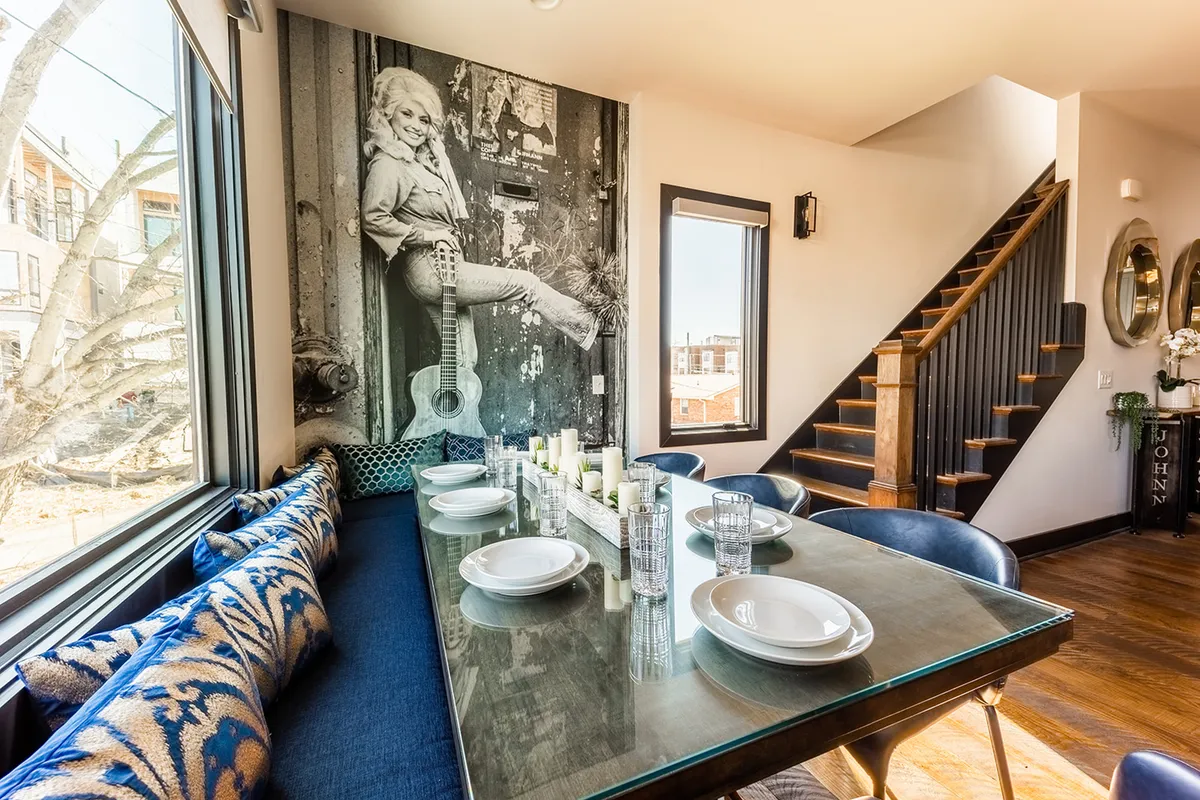 This image showcases a stylish dining area with a large table set beneath a striking mural of a woman with a guitar. The staircase in the background and open arrangement further enhance the sense of flow between the living and dining spaces.