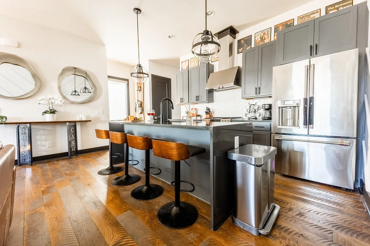 A stylish kitchen interior with an island bar lined with contemporary stools, modern stainless steel appliances, and decorative wall art. The space feels inviting, perfect for both cooking and socializing.
